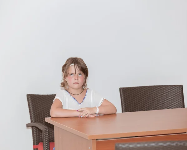 Klein meisje aanbrengen achter de tafel in de klas en opzoeken — Stockfoto