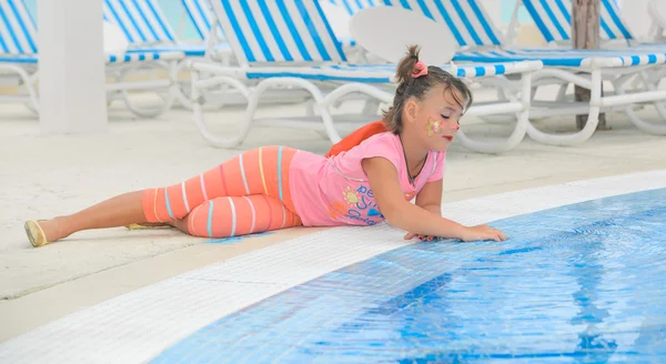 Child laying down at the pool edge and softly touching the water — Stock Photo, Image