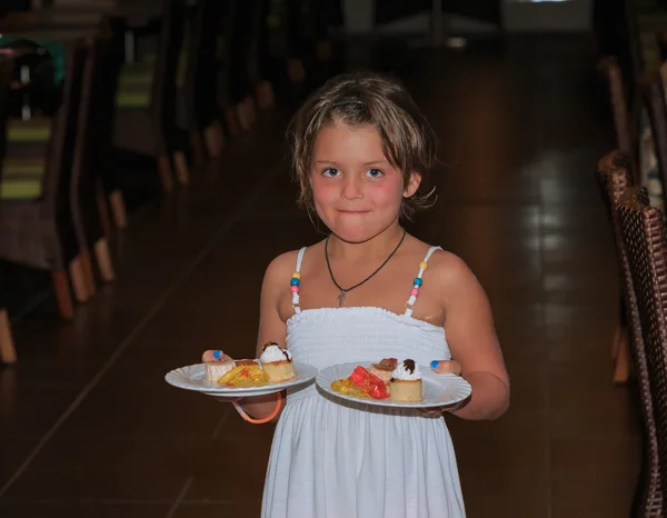 Little girl carrying two ceramic dish plates loaded with various pastries and jello cake pieces — Stock Photo, Image