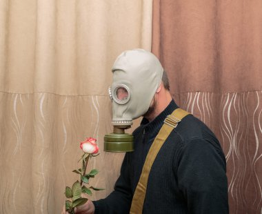 gaz odasında duran ve gül çiçek tutan maskeli insan