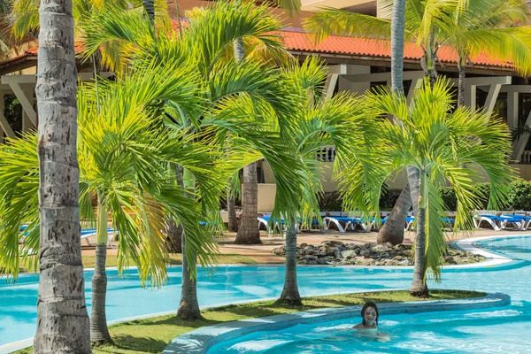 Jardín natural de palmeras esponjosas con niña nadando en la piscina — Foto de Stock