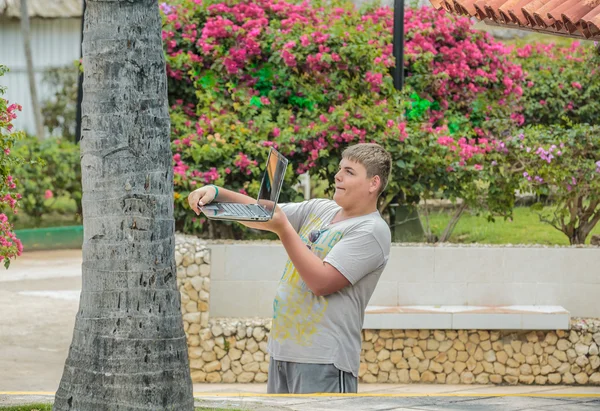 Teenage boy making pictures on his laptop in tropical garden — Stock Photo, Image