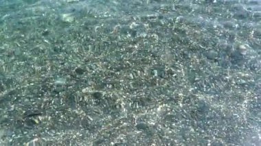 Çakıl taşının altındaki küçük şeffaf deniz dalgaları. Güneş denizin dibinde ve su yüzeyinde parlıyor. En saf deniz suyu. Kopya alanı ile farklı tasarım amaçları için yaz arkaplanı modayı