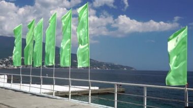 Yalta 'da rüzgarda dalgalanan parlak yeşil bayraklar. Kırım 'ın güney kıyısındaki tatil köyü. Deniz manzaralı dekorasyon. Yaz boyunca Kırım 'da seyahat et. Şehrin ve etrafındaki dağların manzara manzarası