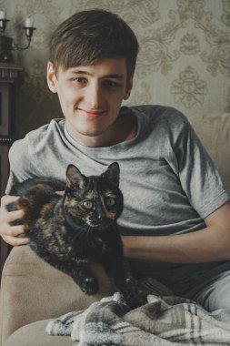 Bir kaplumbağa kabuğu kedisi ve sahibi genç bir adam kanepede oturuyor ve kameraya bakıyor..