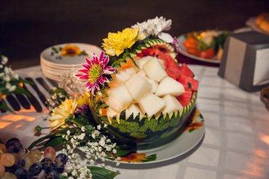 Kavun ve karpuz hamuruyla doldurulmuş taze çiçeklerle süslenmiş oyulmuş karpuz..