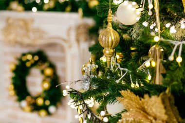 Altın ve gümüş Noel oyuncakları, toplar ve çelenkler noel ağacının ladin dalında bir şöminenin arka planında köknar çelengi ile.
