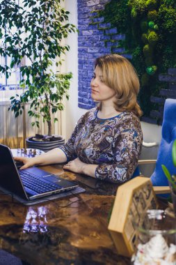 Genç bir kadın iç mimar ofisinde bilgisayar başında çalışıyor. Yeşil ofis, ofis içinde canlı bitkiler, sabitlenmiş yosundan yapılmış bir duvar, epoksi reçine masası.