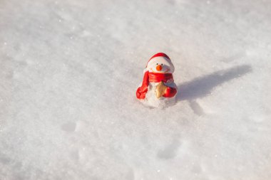 Kardan adam oyuncağı güneşli kış akşamında gün batımında kar örtüsünün üzerinde durur. Kardan adamla minimal kar arkaplanı