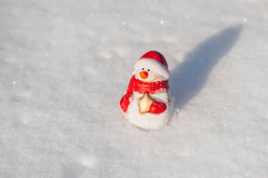 Kardan adam oyuncağı güneşli kış akşamında gün batımında kar örtüsünün üzerinde durur. Kopya alanı olan kardan adam ile minimal kar arkaplanı