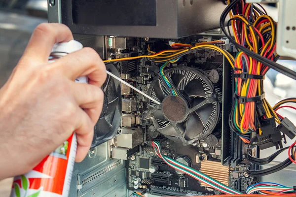 Maintenance and cleaning of the insides of the computer. Mans hand holds a cylinder of compressed air and cleans the insides of the computer