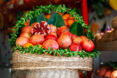 Basket basket decorated with fresh green leaves with juicy ripe pomegranate fruits and oranges prepared for squeezing juice in a street cafe.