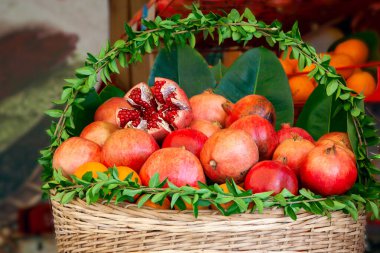 Basket basket decorated with fresh green leaves with juicy ripe pomegranate fruits and oranges prepared for squeezing juice in a street cafe.