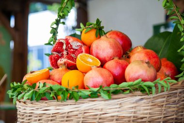 Basket basket decorated with fresh green leaves with juicy ripe pomegranate fruits and oranges prepared for squeezing juice in a street cafe.