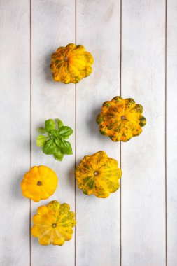 Yellow patissons or squash and a basil leaf on light wooden background top view flatlay