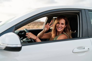 Young woman waving through the window while driving her car