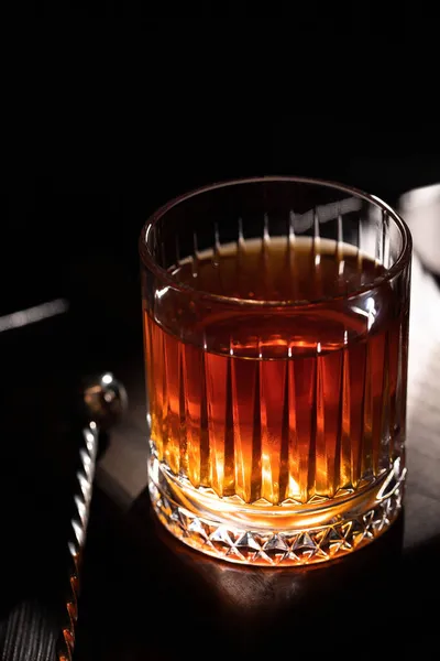 Faceted glass of whiskey with cocktail spoon on a wooden table — Stock Photo, Image