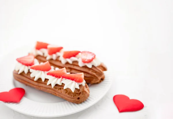 Eclairs with cream and strawberries on a white plate. Valentines Day Concept — Stock Photo, Image