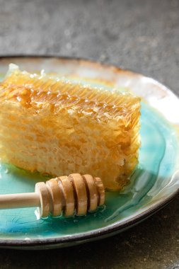 Mühürlenmiş bal peteği ve ahşap bal kovanı beyaz bir masada mavi bir porselen tabakta bal karıştırmak ve tatmak için.