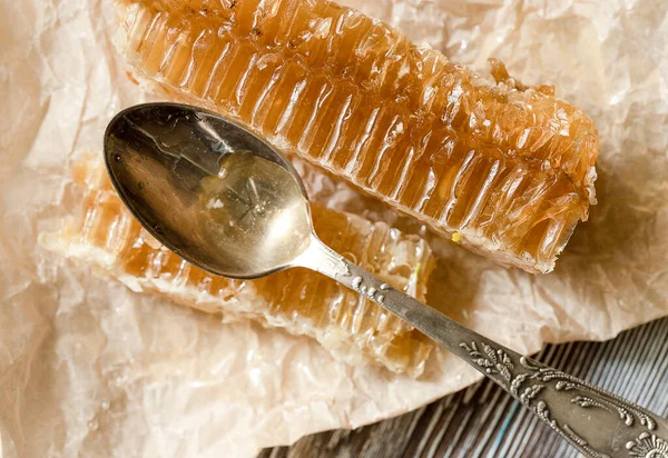 Peigne en nid d'abeille scellée de miel avec petite cuillère en métal sur papier parchemin — Photo