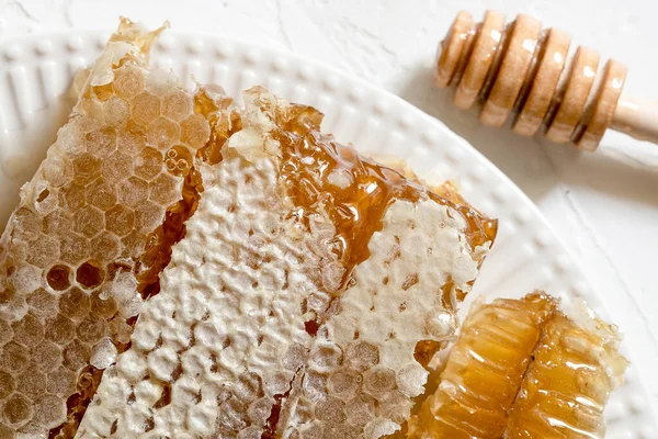 Amidon de miel scellé avec trempette à miel en bois pour mélanger et déguster du miel naturel sur une assiette en porcelaine blanche sur une table blanche — Photo