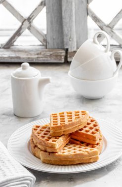 Beyaz porselen tabakta yoğurtlu waffle ve pencere kenarında da siyah gayzer kahve makinesi.