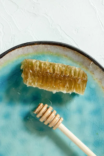 Amidon de miel scellé avec trempette à miel en bois pour mélanger et déguster du miel naturel sur une assiette en porcelaine bleue sur une table blanche — Photo