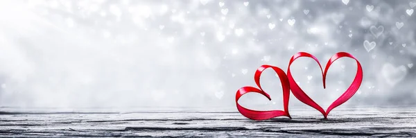 Dvě Červené Stuhy Srdce Dřevěném Stole Stříbrným Pozadí Bokeh Valentýna — Stock fotografie