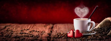  Espresso bardağı ve kalp şeklinde buharlı çay tabağı ve tahta masada kırmızı kalpler.