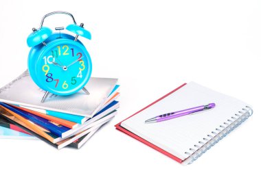 Eğitim veya iş dünyası kavramı: Mavi alarm saati bir defter ve kalem moru ile birlikte bir yığın kitabın üzerine yerleştirilir.