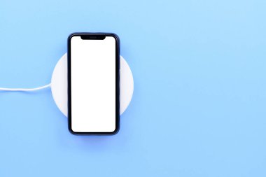Siyah cep telefonu beyaz kablosuz şarj cihazını mavi pastel arka planda kullan