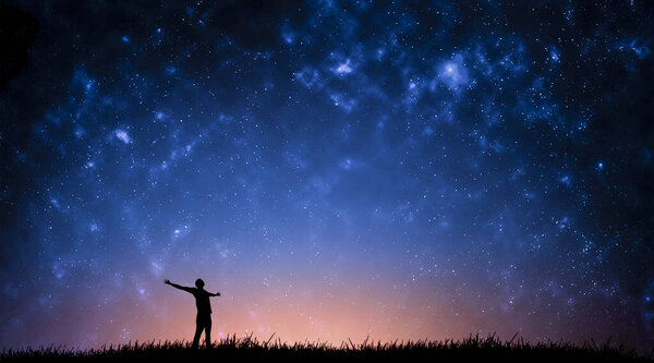 Night landscape with Milky Way. Silhouette of a standing young man with raised up arms on the mountain. Beautiful Universe. Travel background with blue night starry sky.
