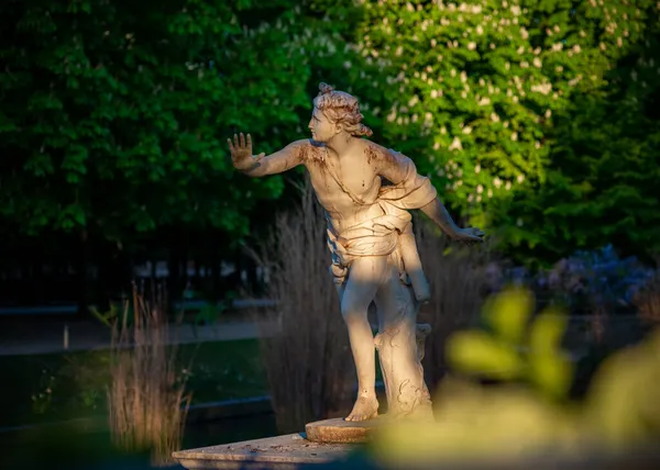 Paris 'teki Tuileries bahçesinde 18. yüzyıl tanrıçası heykeli. Arka planda çiçek açan kestane ağaçları var. Güneşli bir bahar sabahı çekilmiş.