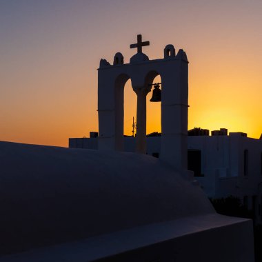 A traditional church steeple at sunset in the Aegean Island of Ios, Greece, with orange sky and no people. Taken at the end of a perfectly sunny summer day.