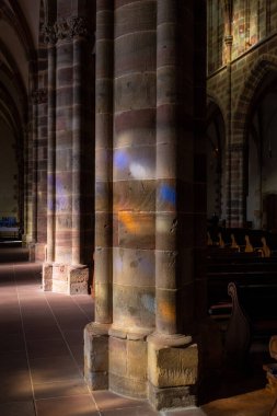 Various colors from stained glass projected on pillars in St. Peter and St. Paul abbey located in Wissembourg, France, with no people