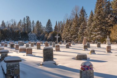 Kışın Saint-Adolph-d 'Howard, Quebec' te güneşli bir günde karla kaplı bir haç ve mezar taşı bulunan Kanada mezarlığı.