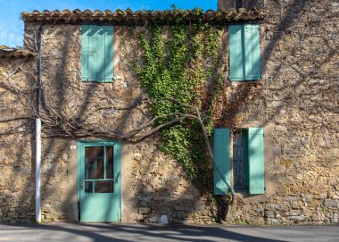 A typical derelict building facade with closed shutters in a Southern France village, with no people, taken on a sunny end of winter day