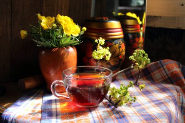 Şeffaf bardakta siyah çay. Kırsal tarzda. Sarı çiçekler. Genç dallar. Bir fincan çay. Ahşap dekor. Havan topu ve tokmak.