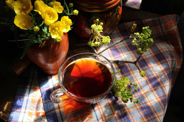 Şeffaf bardakta siyah çay. Kırsal tarzda. Sarı çiçekler. Genç dallar. Bir fincan çay. Ahşap dekor. Havan topu ve tokmak.
