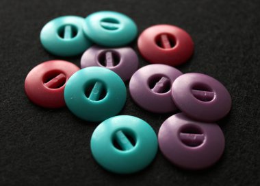 Alışılmadık dizayn düğmeleri dikiyorum. Yeşil, mor ve kırmızı düğmeler. Siyah arkaplanda aksesuarlar dikiliyor. 