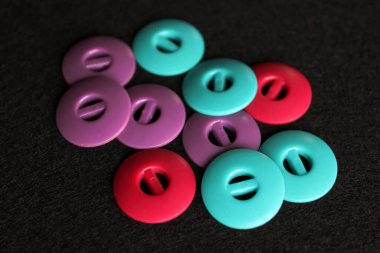 Alışılmadık dizayn düğmeleri dikiyorum. Yeşil, mor ve kırmızı düğmeler. Siyah arkaplanda aksesuarlar dikiliyor.