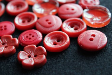 Farklı şekil ve boyutlarda kırmızı dikiş düğmeleri. Siyah arka planda aksesuarlar dikmek. Giysiler için düğmeler. Klasik plastik düğmeler. 