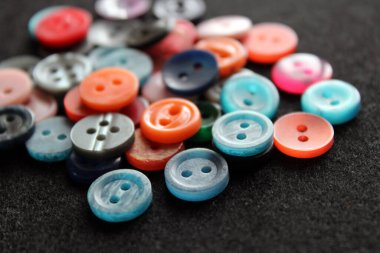 Çok renkli plastik dikiş düğmeleri. Mavi, pembe ve gri düğmeler. Siyah arkaplanda aksesuarlar dikiliyor. 