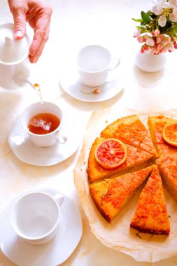 Üç kişilik tatlı kekli çay partisi. Eski bardaklar, çay tabakları ve bahar pembesi çiçekleriyle süslenmiş.