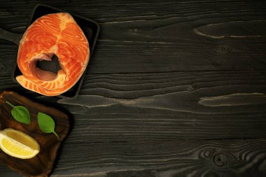 Mutfak masasının ahşap yüzeyinde limonlu, fesleğenli ve yağlı somon bifteği taze otlarla deniz ürünleri pişiriyorum.