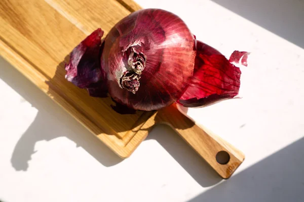 Sıcak güneş ışığı altında tahta bir tahtanın üzerinde kırmızı soğan.