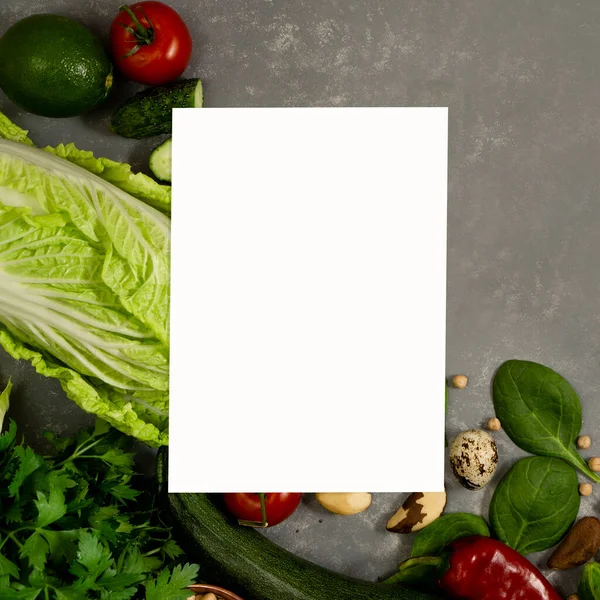 Diet plan with greens and fresh vegetables in a paper notebook on a gray table surface.