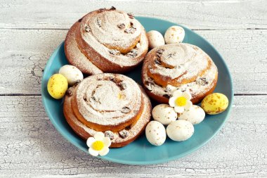 Şeker çiçekli Paskalya dekoru ve mavi tabakta yuvarlak spiral çöreklerle çikolatalı yumurtalar.