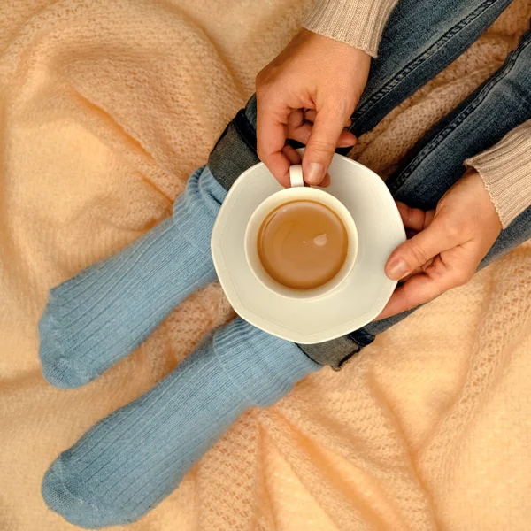 Coffee with milk in the comfort of a warm blanket.Coffee with milk in the comfort of a warm blanket. Woman in blue socks and jeans with a cup of coffee in her hands on a knitted shawl