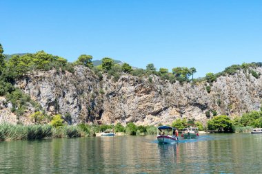 Türkiye 'nin güneybatı kıyısındaki Marmaris ve Fethiye ilçeleri arasında yer alan Mugla ilindeki Lycian mezarlarının bulunduğu kayaların yanındaki Dalyan Nehri' nde turistik zevk tekneleri.
